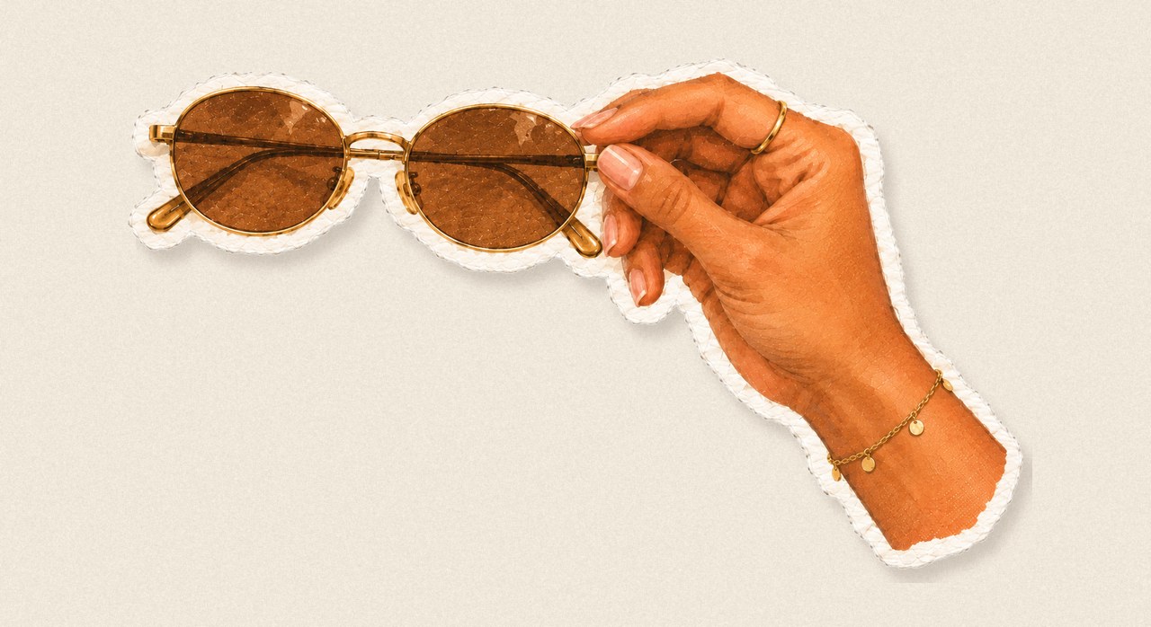 Small oval gold-rimmed sunglasses held in a hand
